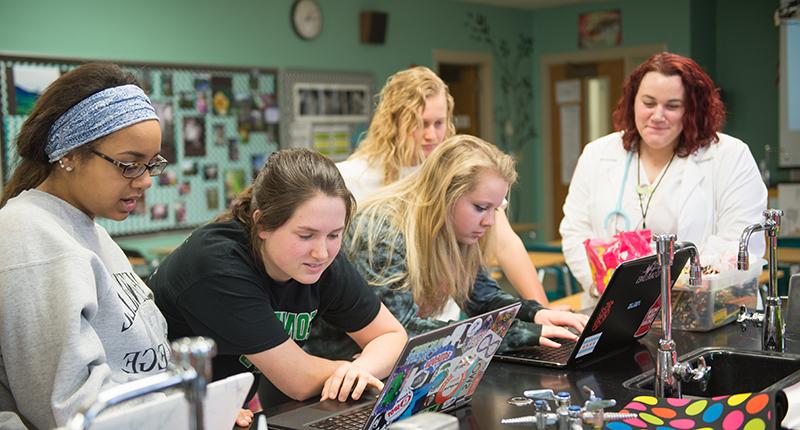 Four girls in a college of nursing lab looking at computers.